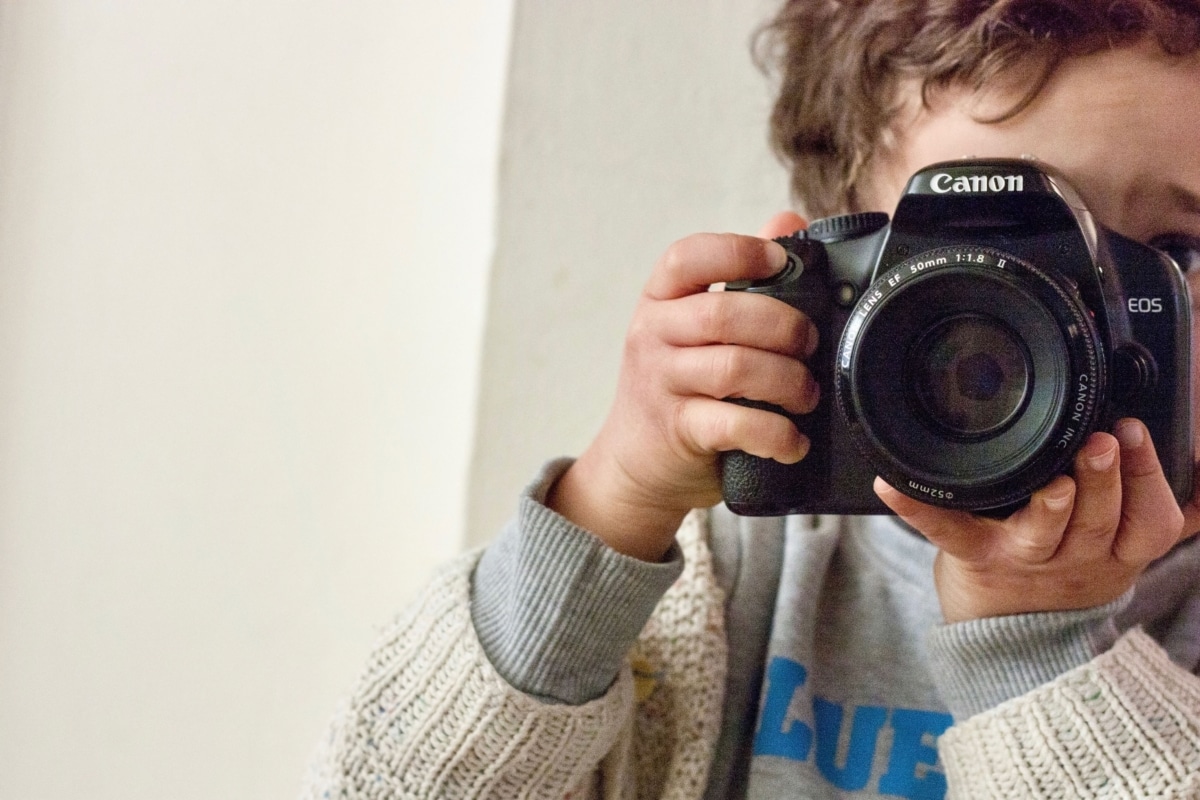Ein Kind hält eine Kamera in den Händen. Der Umgang mit Fotos in der Kita sollte mit Eltern und im Team thematisiert werden.